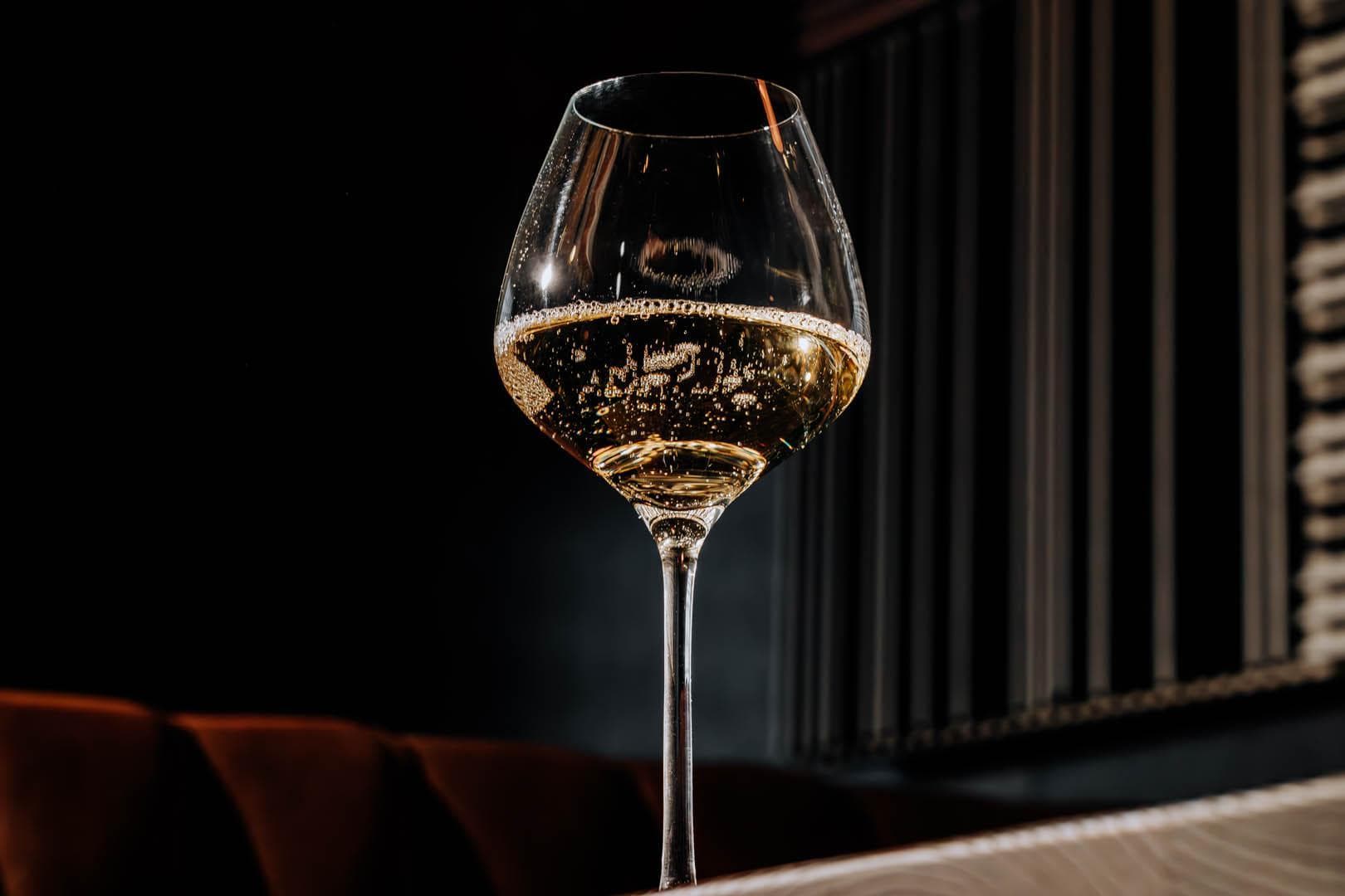 A glass of champagne on a table in a dimly lit setting.