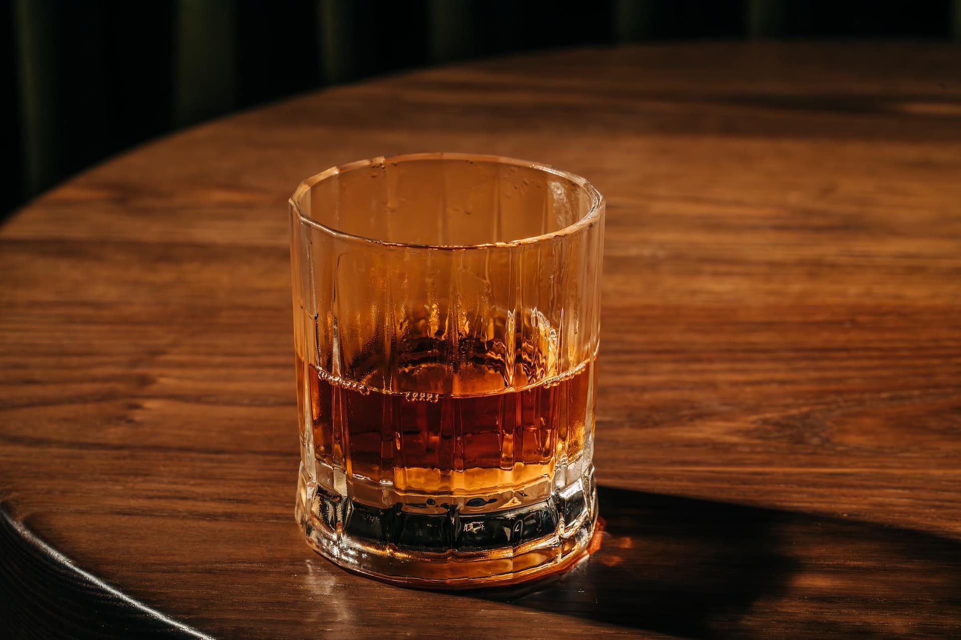 A glass of amber-colored cocktail is placed on a wooden table.