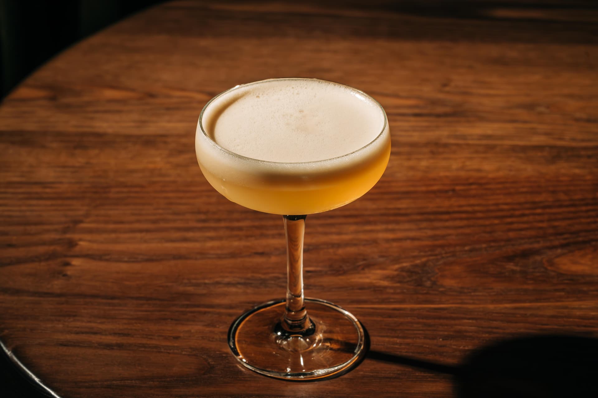A frothy cocktail presented in a coupe glass, placed on a wooden table.