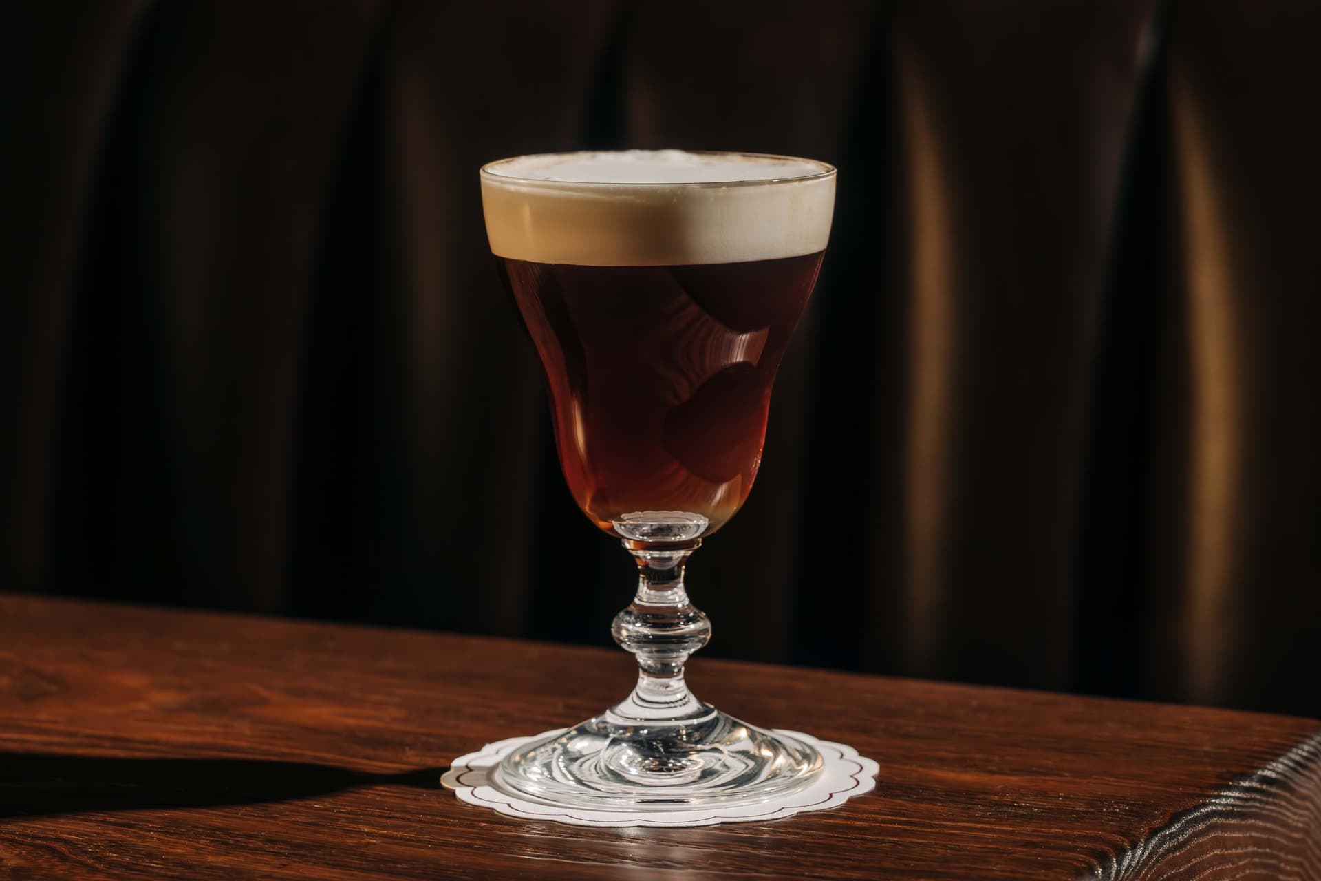 A glass of Irish coffee sits on a wooden table, with a frothy cream layer on top.