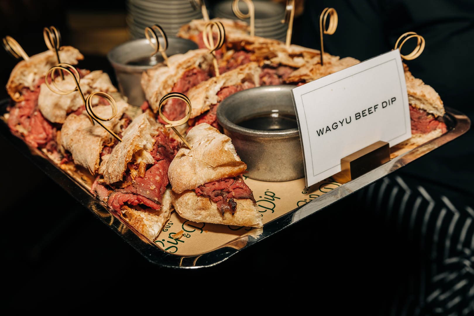 A tray of Wagyu beef dip sandwiches neatly arranged with a sign identifying the dish.