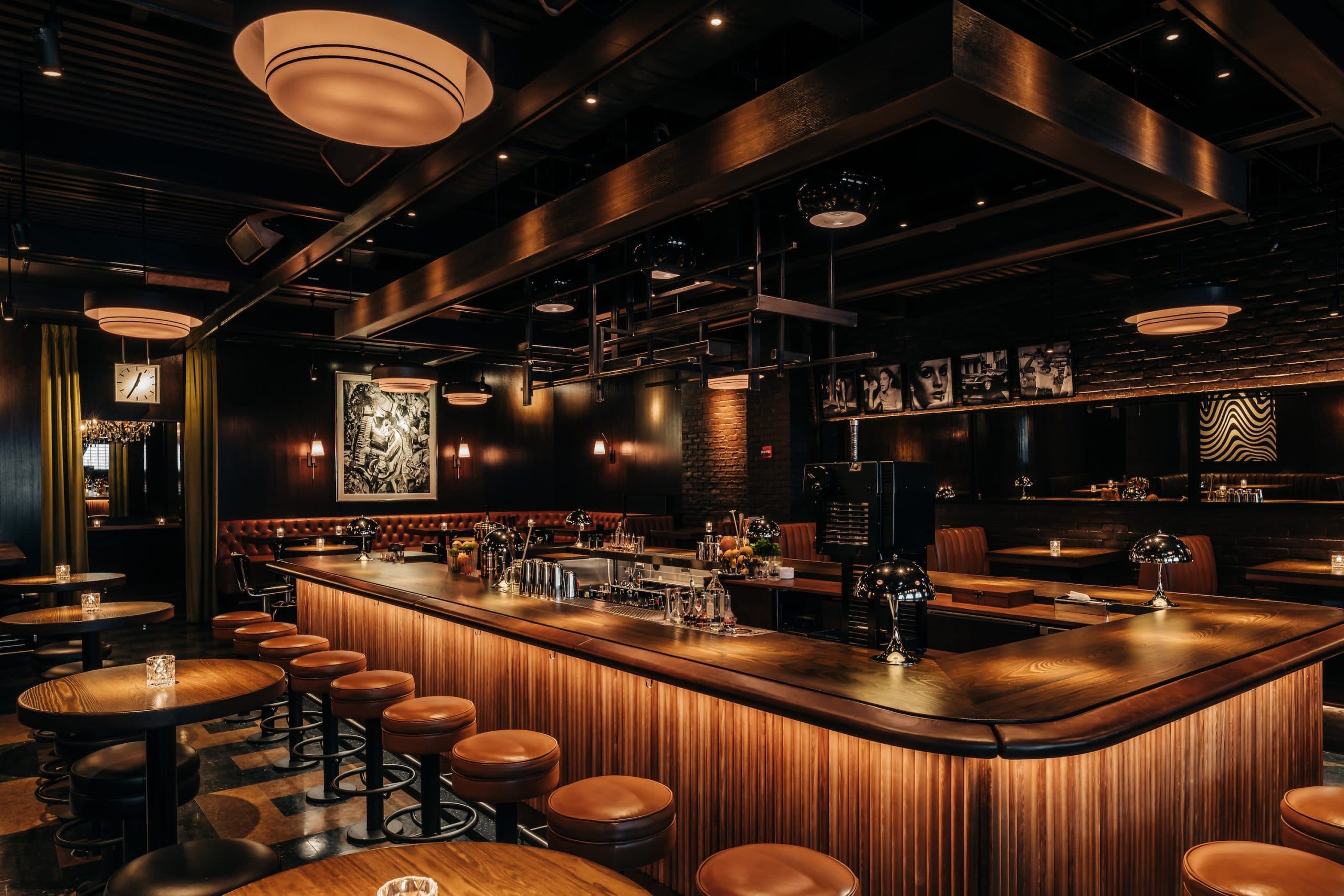 Interior of Gus' Sip & Dip bar with a long wooden counter, round stools, ambient lighting, and contemporary decor.